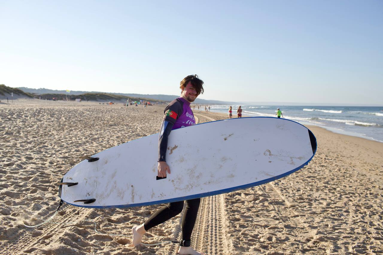 A smiling participant carrying a surfboard along the beach